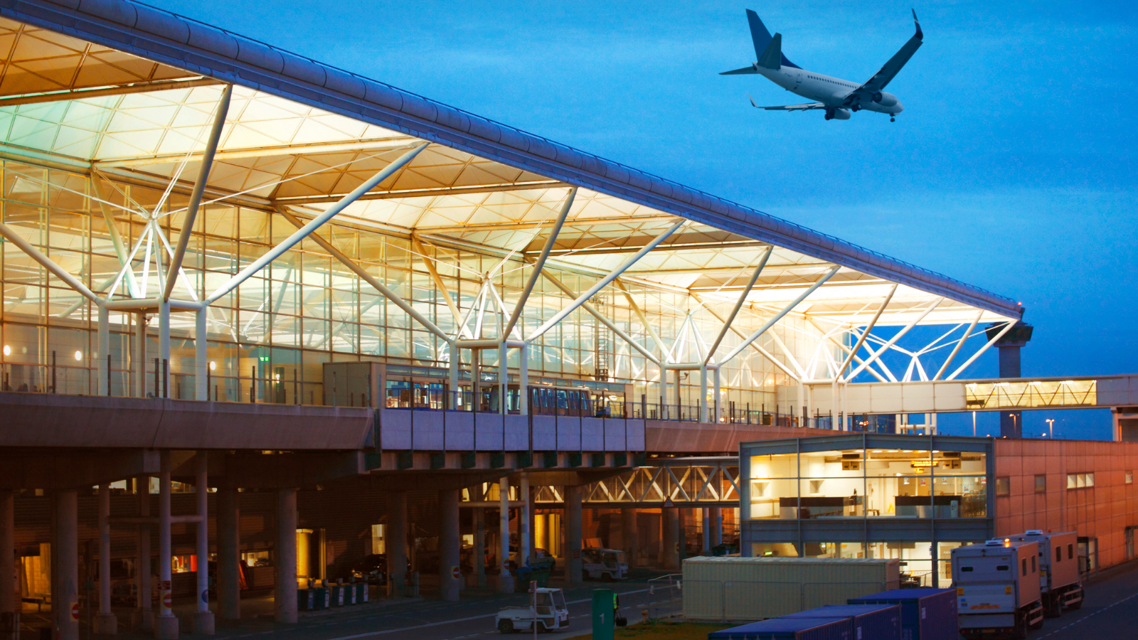 An image of Stansted Airport with an aeroplane flying above in the sky.