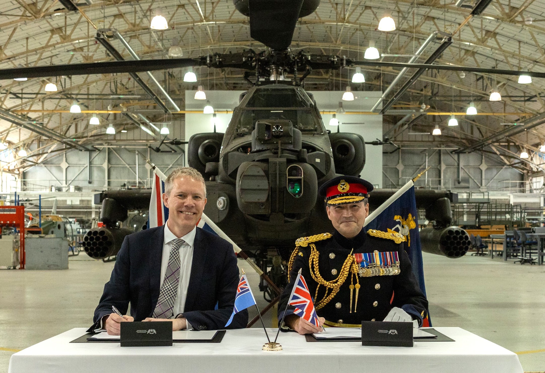 Image of two men sitting at a table with the UK Civil Aviation ensign and UK flags on the table signing an agreement